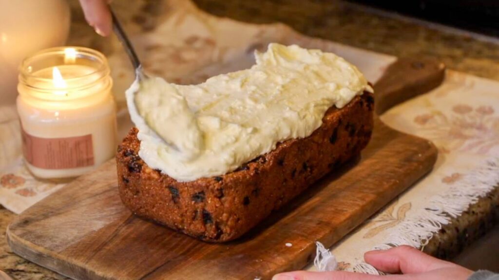 Spreading cream cheese frosting over a freshly baked carrot cake loaf.