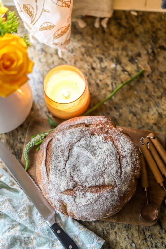 Whole grain sourdough buttermilk bread loaf on a cutting board with a knife and candle