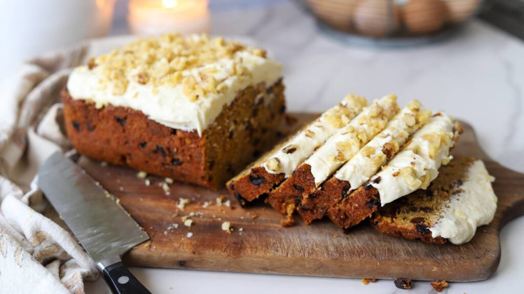 Sliced carrot cake loaf with cream cheese frosting on a wooden board.