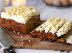 Sliced carrot cake loaf with cream cheese frosting on a wooden board.