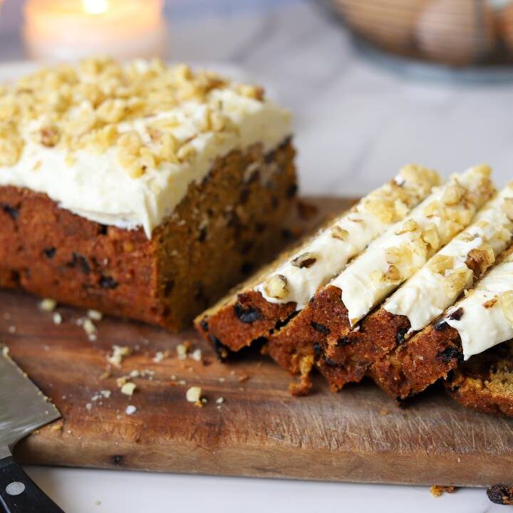 Sliced carrot cake loaf with cream cheese frosting on a wooden board.
