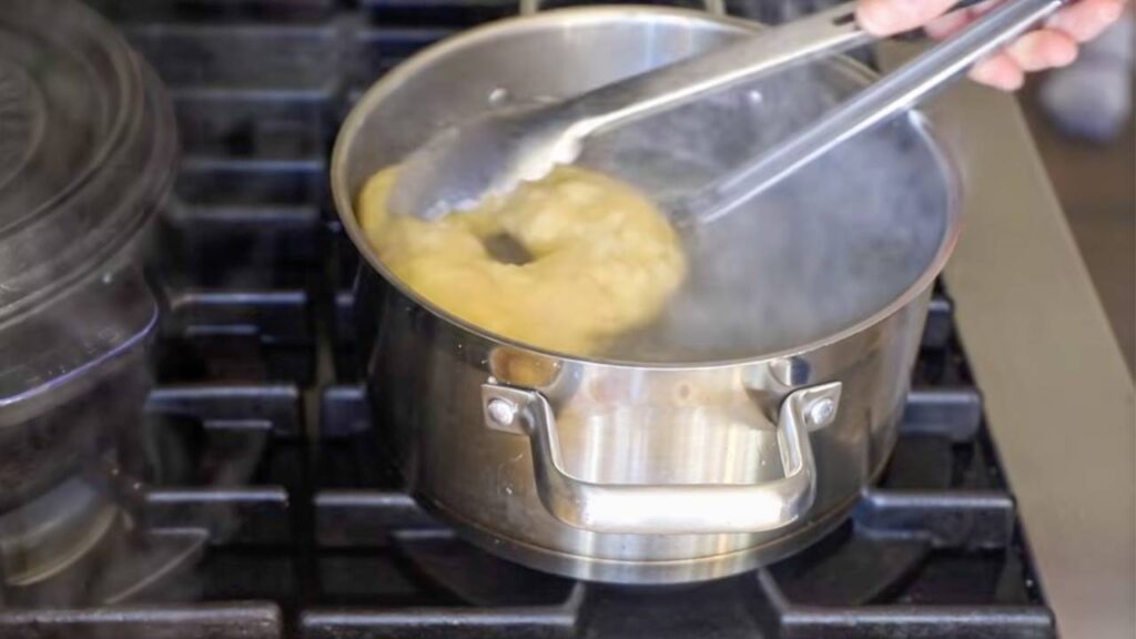 Boiling sourdough bagel dough in pot before baking