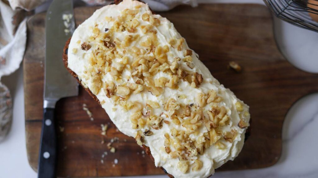 Overhead view of carrot cake loaf topped with cream cheese frosting and chopped walnuts.