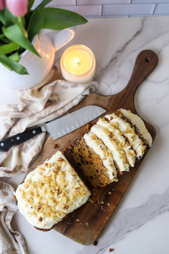 Sliced whole wheat carrot cake loaf with cream cheese frosting on a wooden cutting board.