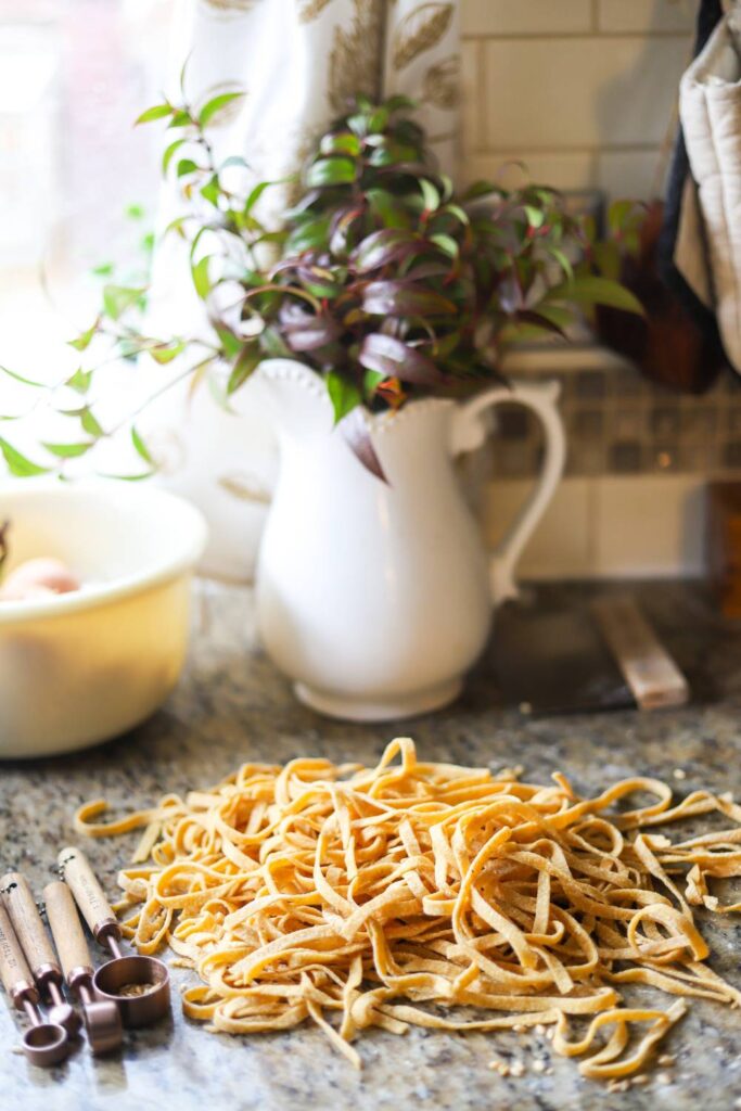Homemade whole wheat pasta noodles on kitchen counter with measuring spoons