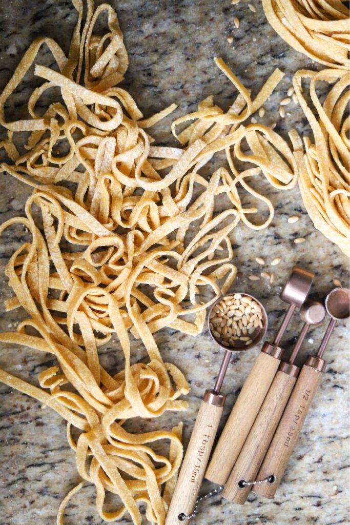 Fresh whole grain pasta noodles with measuring spoons on marble countertop
