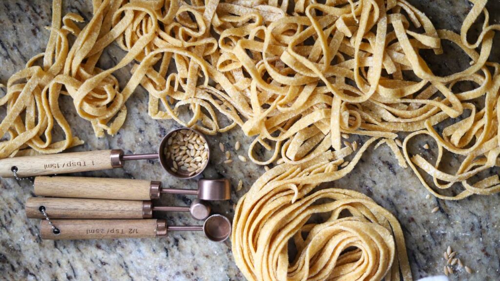 Homemade whole grain pasta noodles with measuring spoons on counter