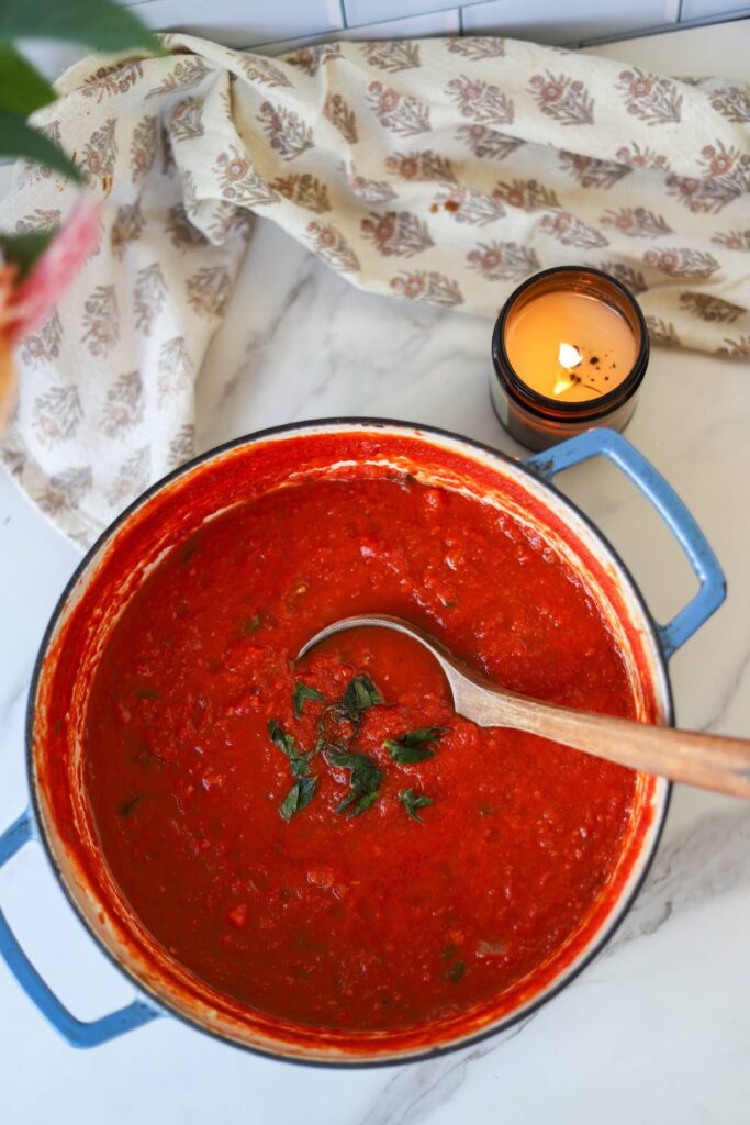 Pot of rustic tomato basil pasta sauce on kitchen counter with flowers and candle