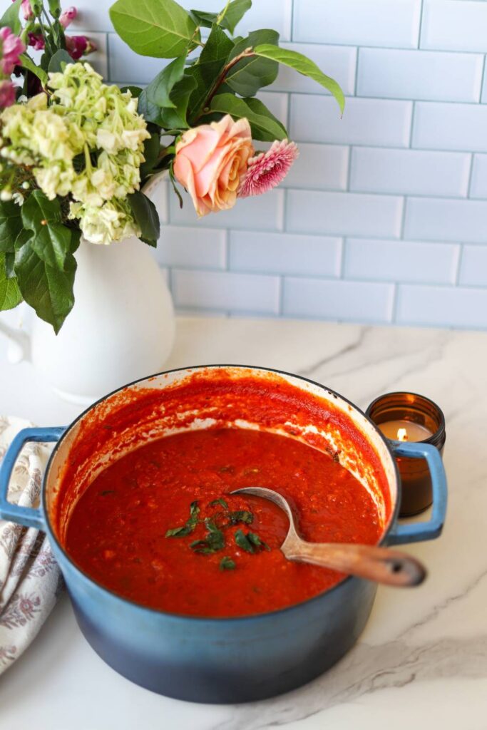 Rustic tomato basil pasta sauce in pot with spoon on marble counter
