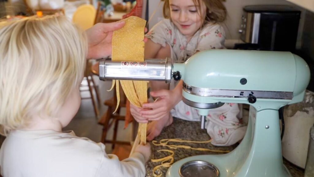 Children watching fresh whole wheat pasta noodles come through mixer