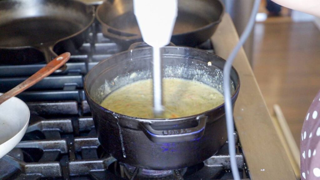 Healthy broccoli cheddar soup blending in a pot on the stove