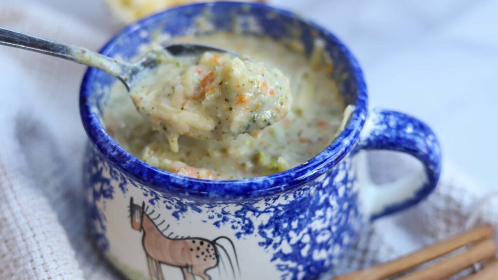 Spoon lifting creamy broccoli cheddar soup from bowl