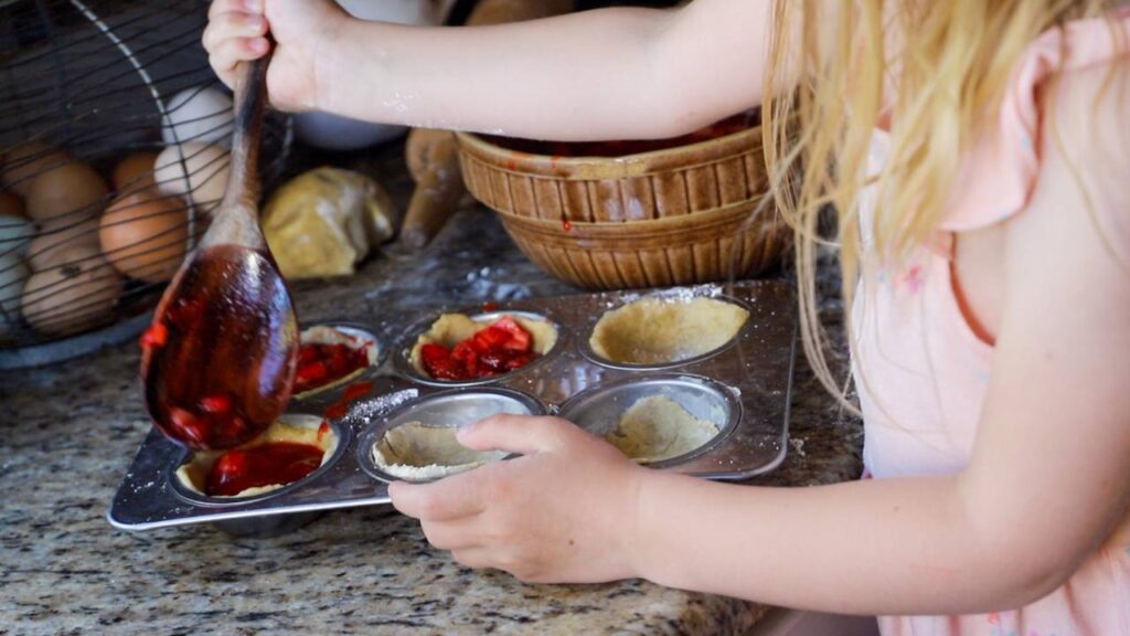 Child filling mini pie crusts with fresh strawberry filling