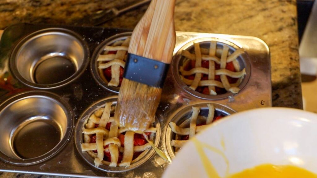 Brushing egg wash over lattice crust on mini strawberry pies