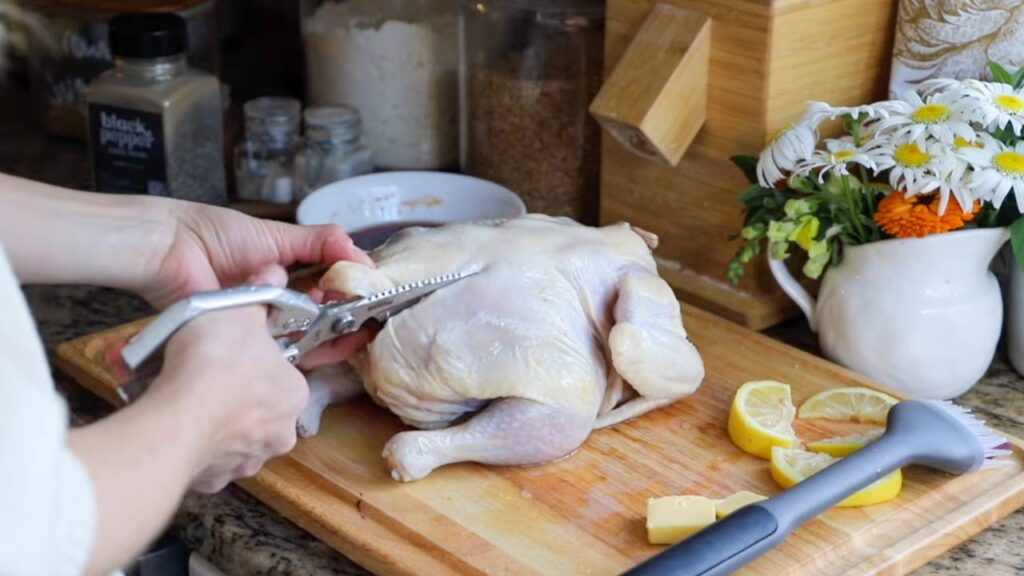 Cutting along the backbone of a whole chicken with kitchen shears.