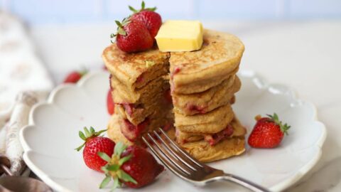Whole grain einkorn strawberry pancakes served with butter, maple syrup, and fresh strawberries.