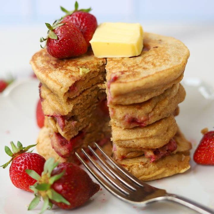 Whole grain einkorn strawberry pancakes served with butter, maple syrup, and fresh strawberries.