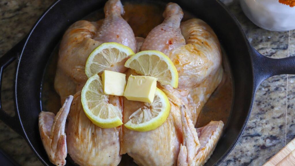 Spatchcock chicken in a cast iron skillet topped with butter and lemon slices.