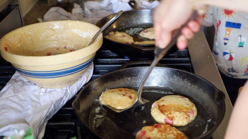 Cooking whole grain einkorn strawberry pancakes in a cast iron skillet.