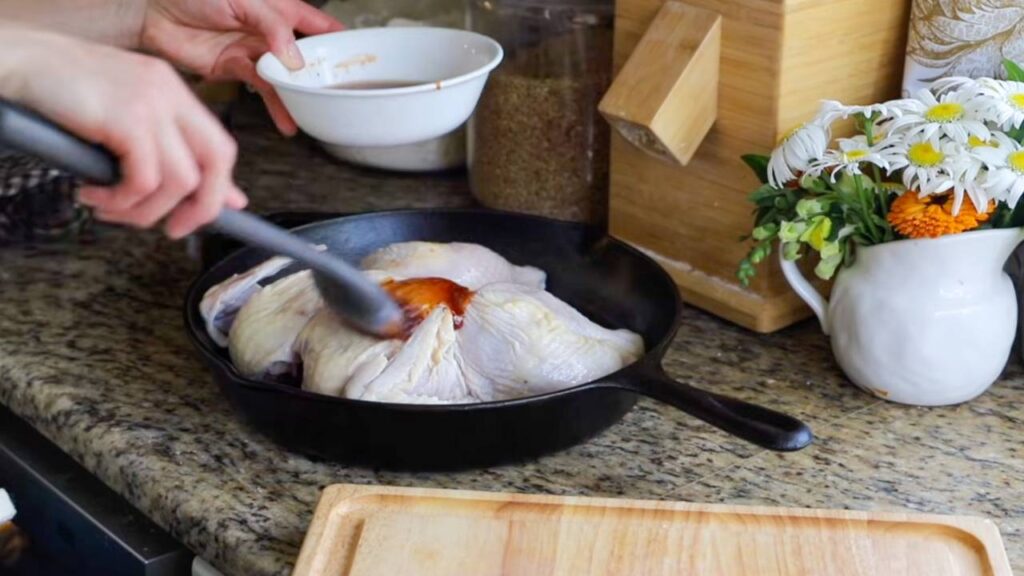 Brushing maple BBQ glaze over a spatchcock chicken in a cast iron skillet.