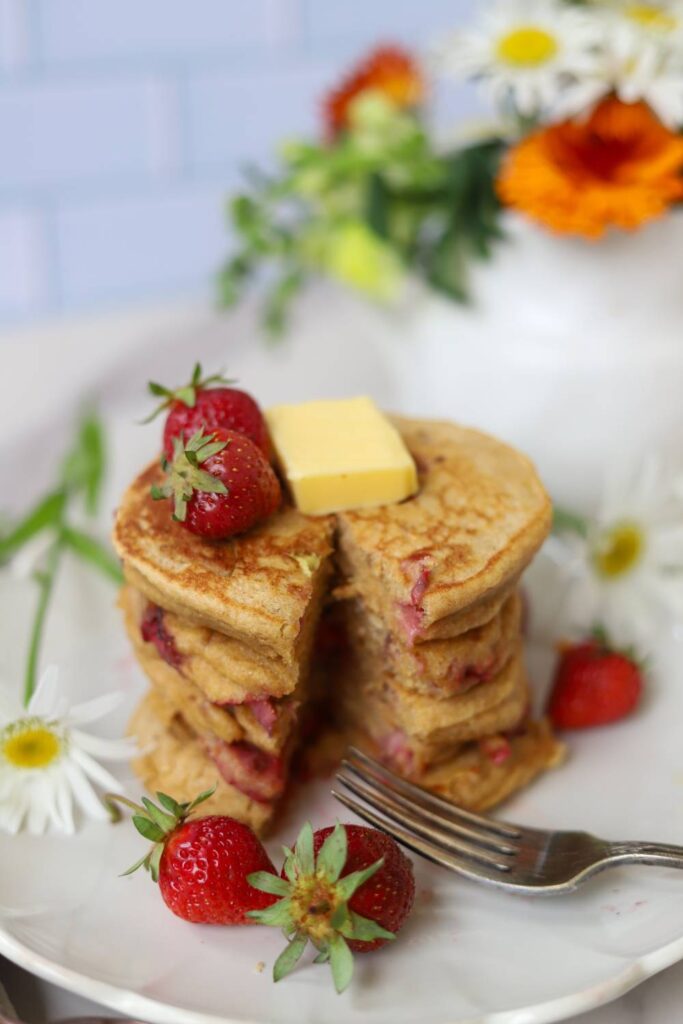 Stack of whole grain einkorn strawberry pancakes with butter and fresh strawberries.