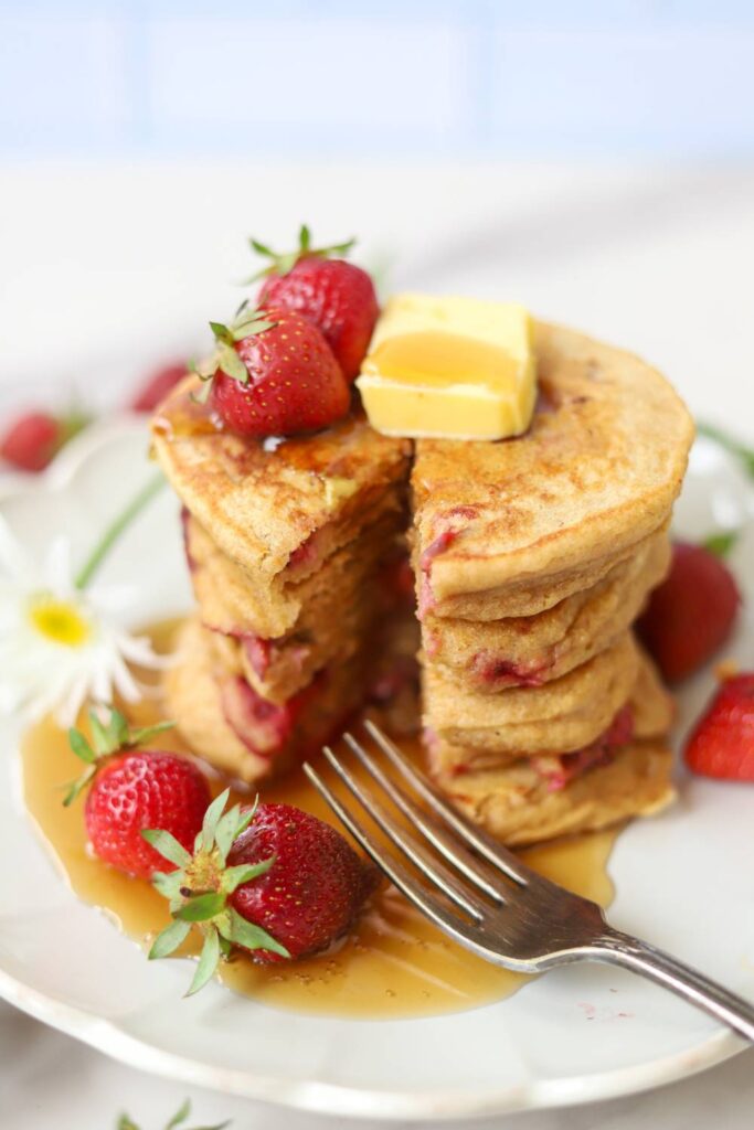 Whole grain einkorn strawberry pancakes topped with butter, maple syrup, and fresh strawberries.