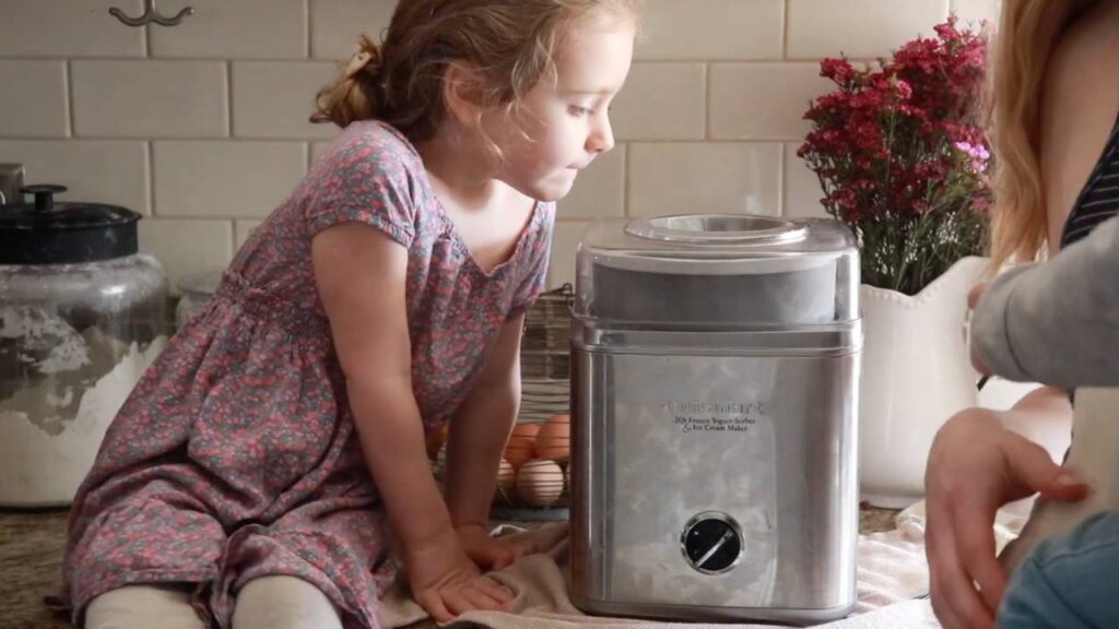 Homemade strawberry ice cream in an ice cream maker with a child nearby