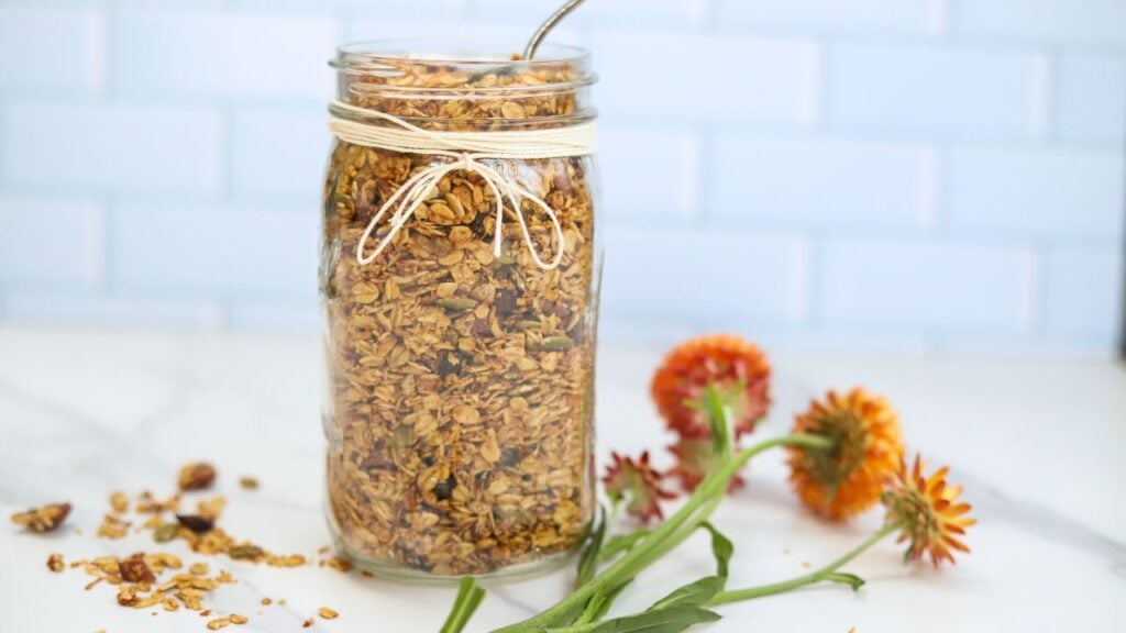 Jar of homemade pumpkin spice granola with a spoon and fall flowers