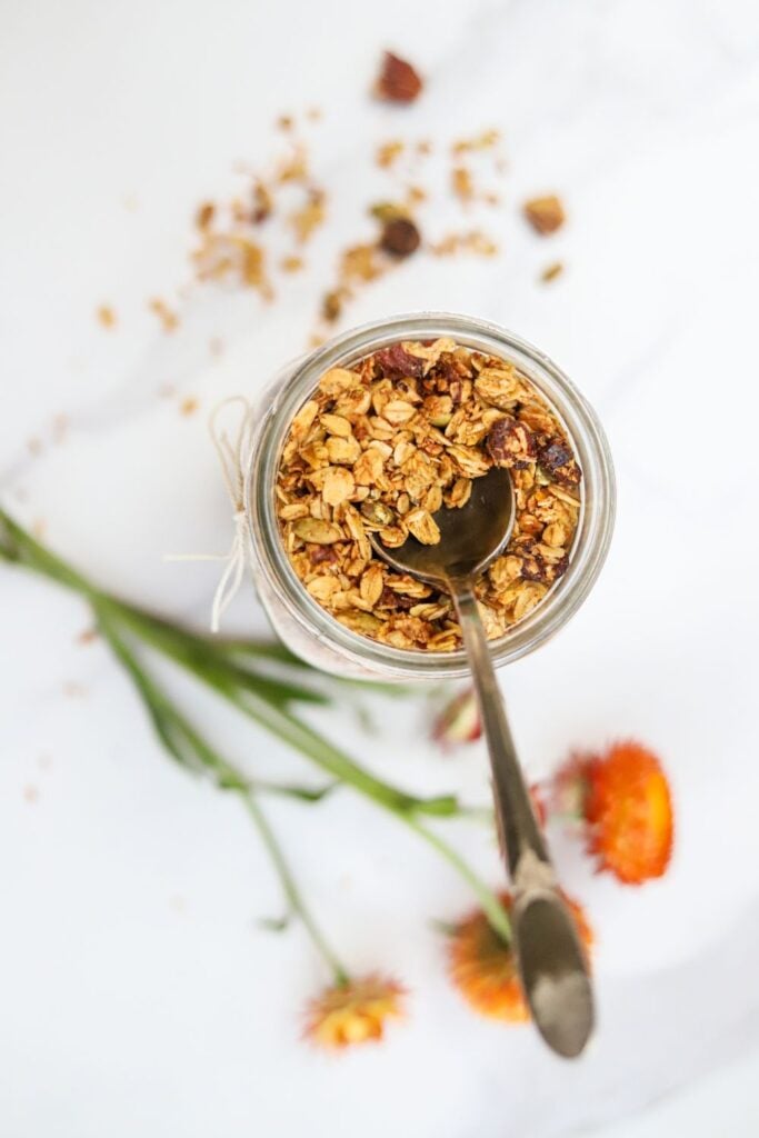Jar of homemade pumpkin spice granola served with a spoon and fall flowers