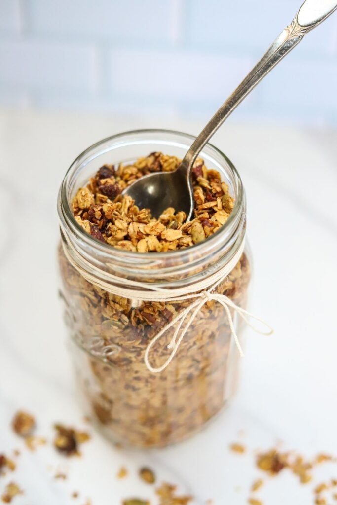 Jar of homemade pumpkin spice granola served with a spoon and fall flowers