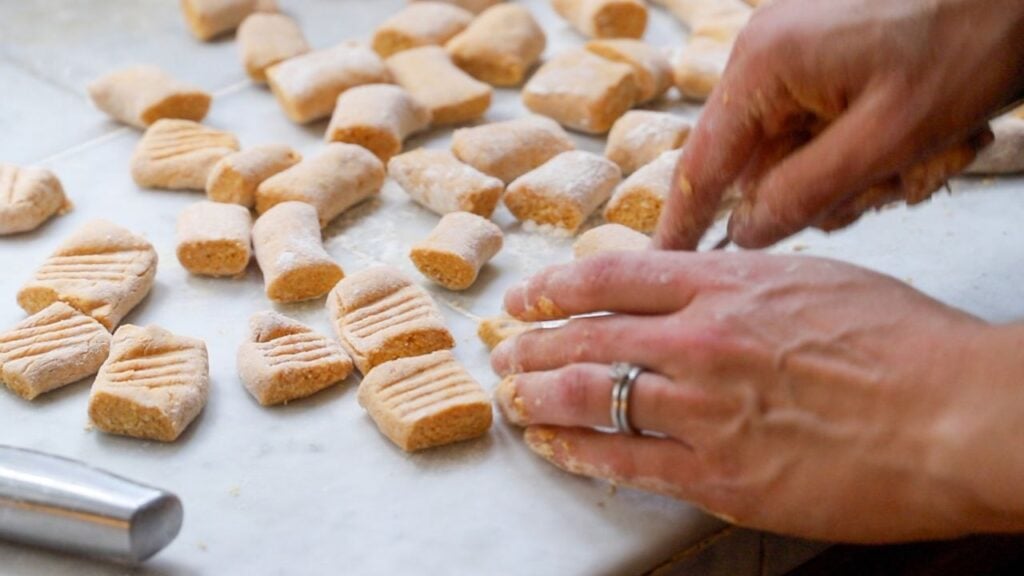 Hands shaping homemade pumpkin gnocchi on a floured counter.