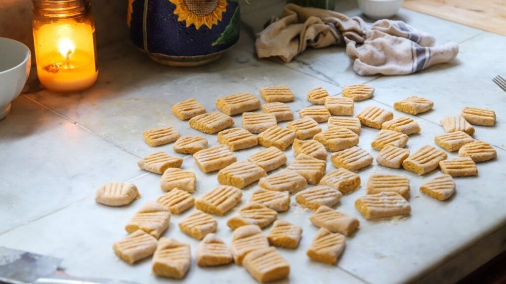 Homemade pumpkin gnocchi arranged on a floured countertop.