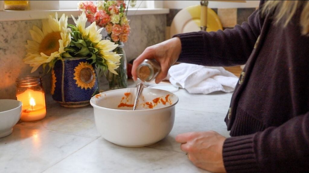 Adding spices to pumpkin gnocchi mixture in a white bowl.