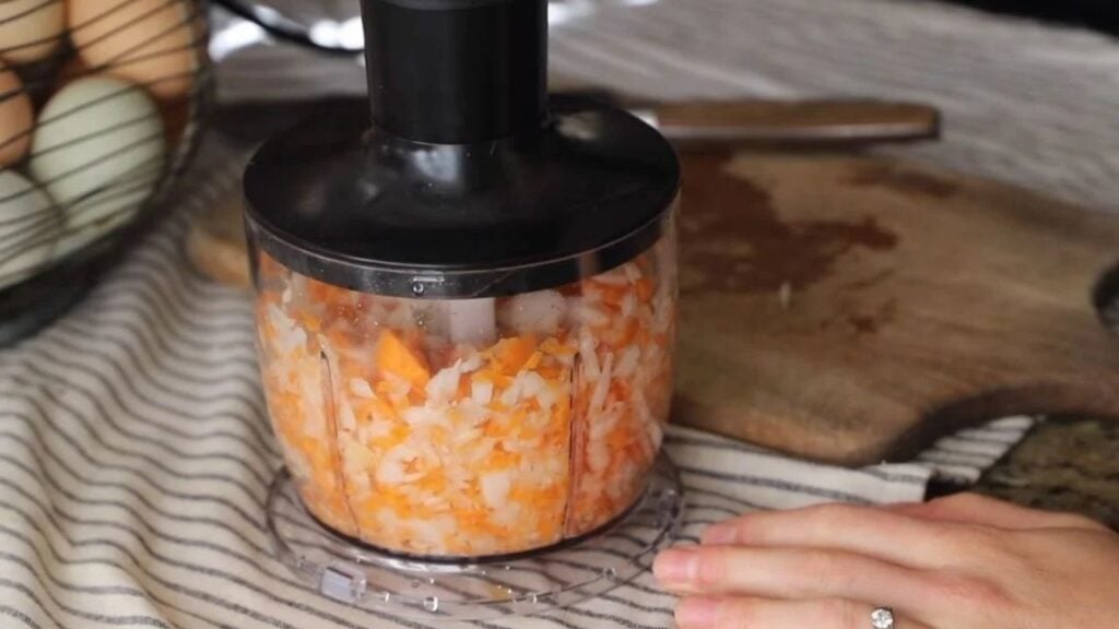 Immersion blender with food processor attachment chopping fresh vegetables.